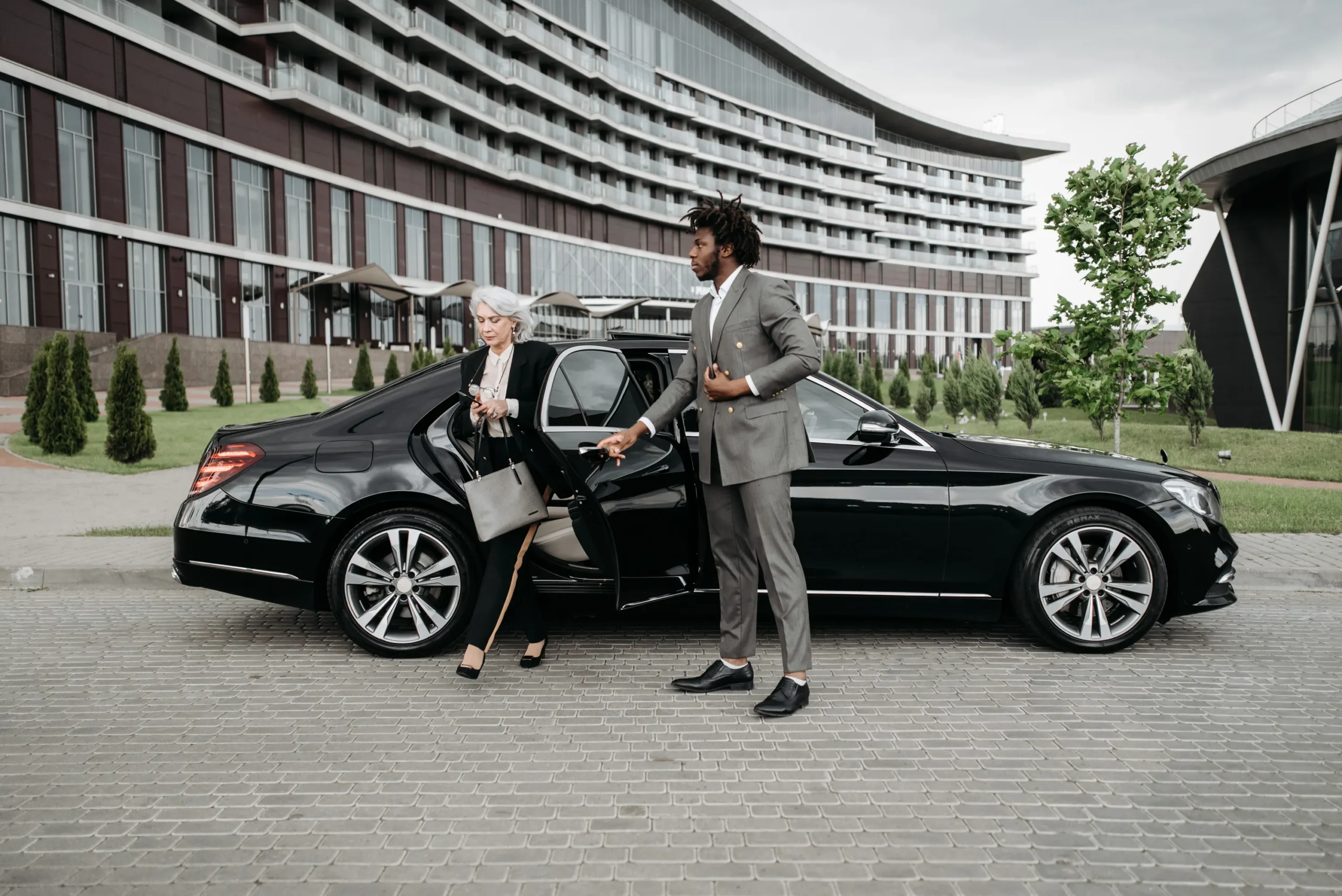 Chauffeur holding the rear door of a black Mercedes-Benz S-Class as an executive steps out at a hotel