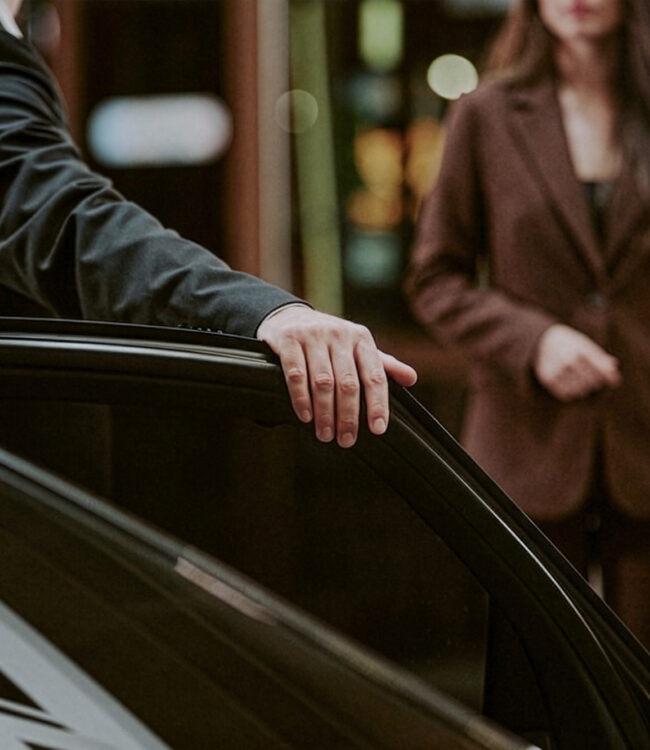 Services 1 Chauffeur holding the rear door of a black car open for a passenger